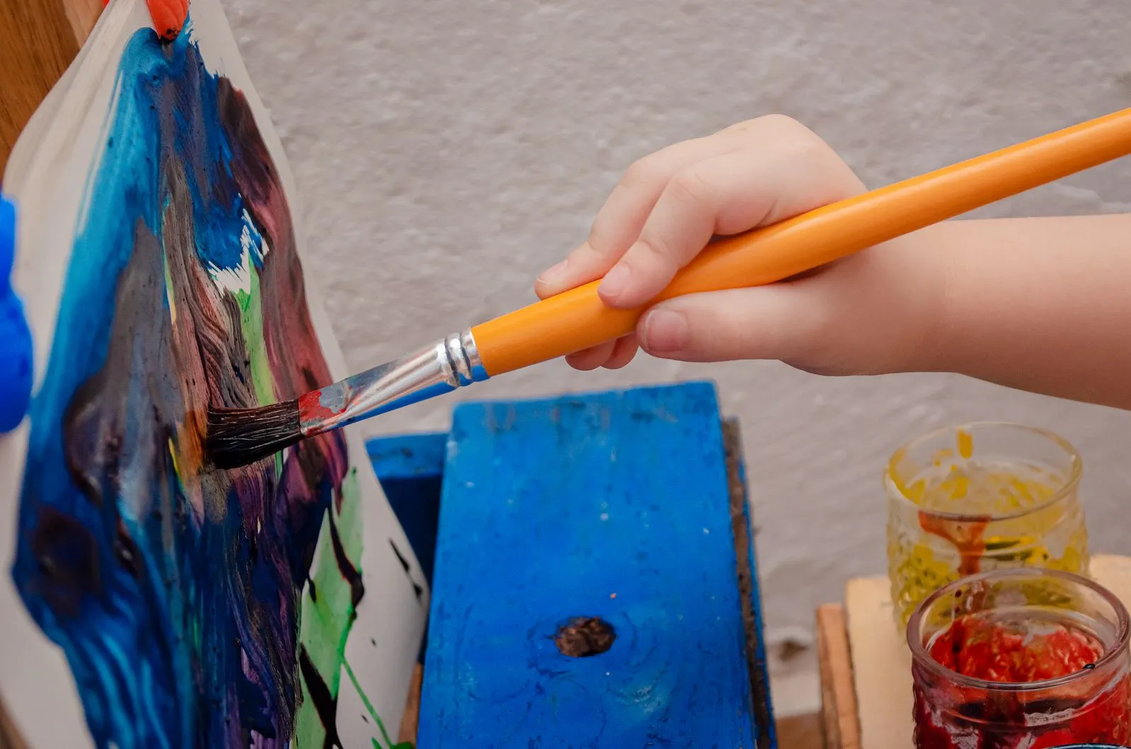 A child uses a brush to create artwork on canvas, showcasing creativity and expression.